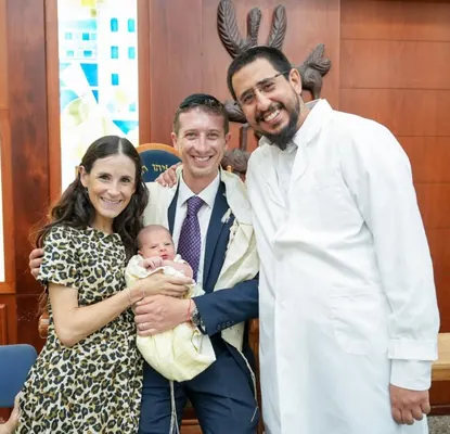 איתמר חמו בחלוק לבן עם משפחה מחייכת והתינוק בבית הכנסת