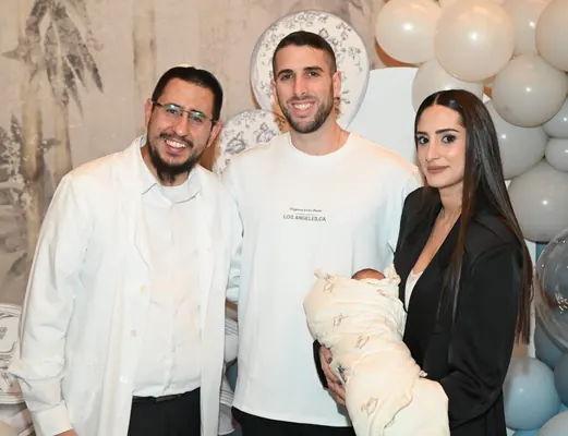 איתמר חמו עם זוג הורים מחייכים והתינוק העטוף, בלונים ברקע