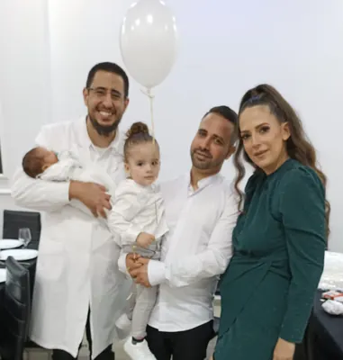 המוהל איתמר חמו מחזיק את התינוק לצד משפחה מחייכת עם בלון לבן