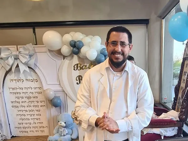 המוהל איתמר חמו בחלוק לבן, מחייך, בברית מילה